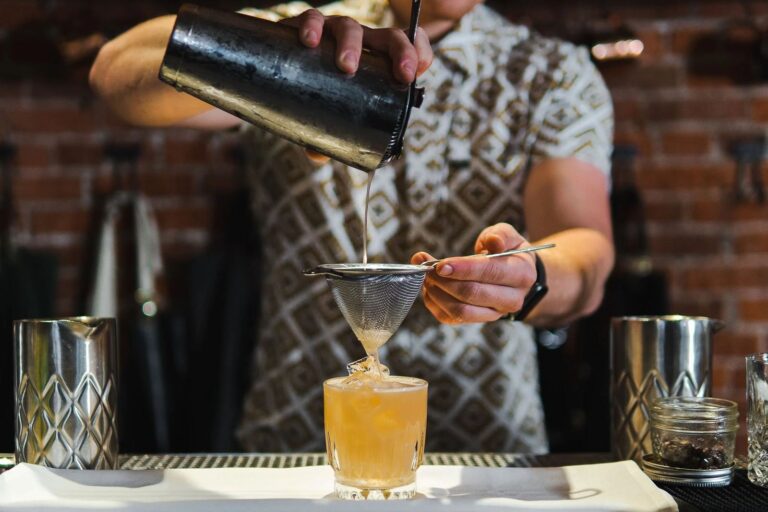 A bartender straining a cocktail into a glass behind the bar