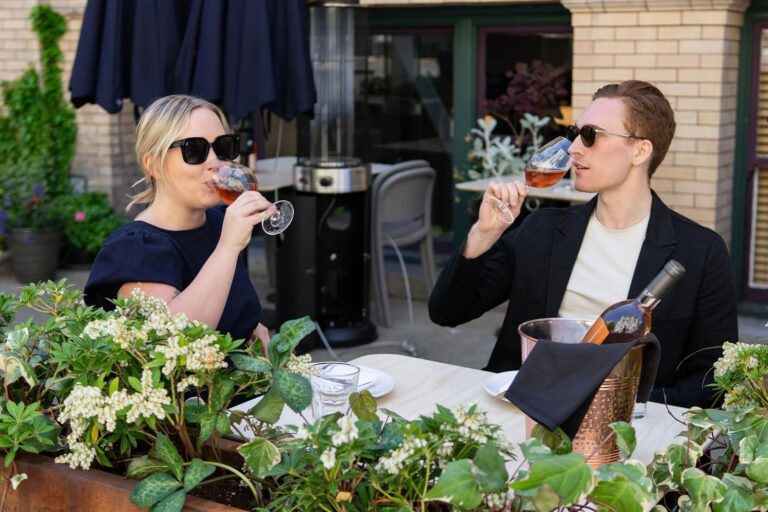 Two guests sitting outside on the patio in the sun, surrounded by planters