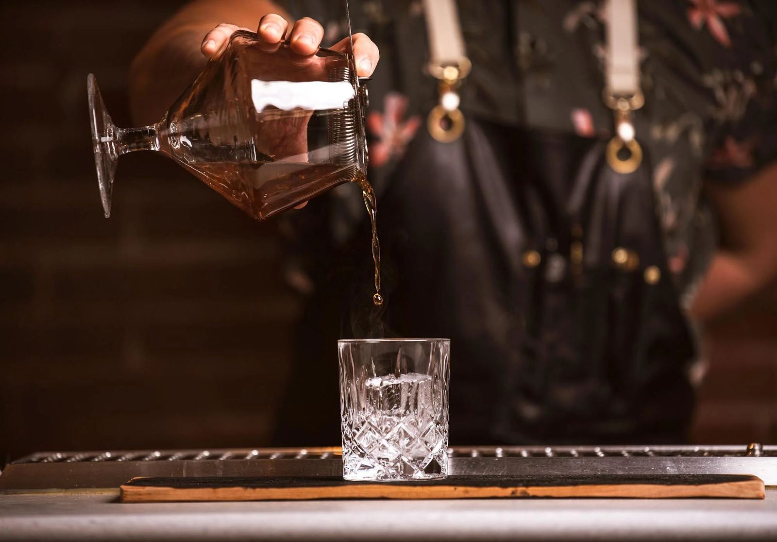 A cocktail being poured into a cut crystal glass at the bar