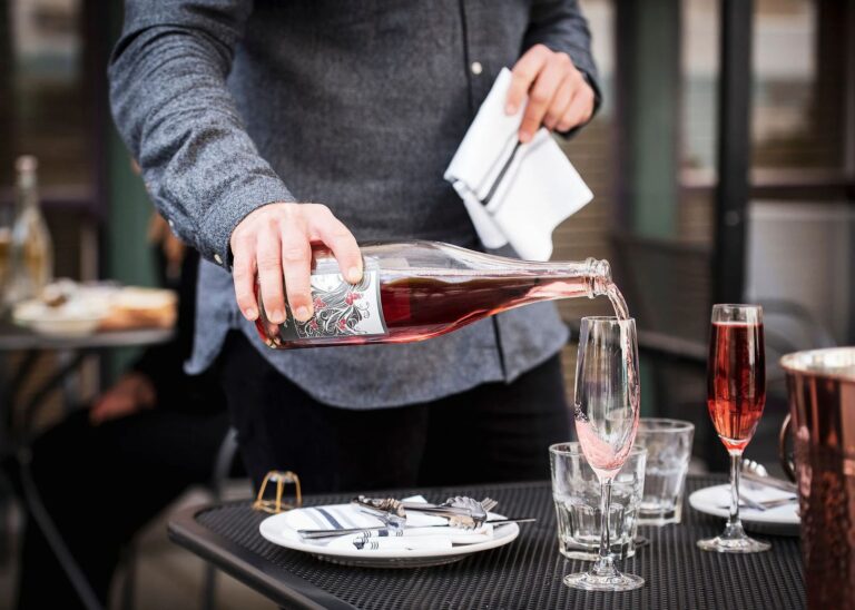 A server pouring red wine into a glass at a candlelit table